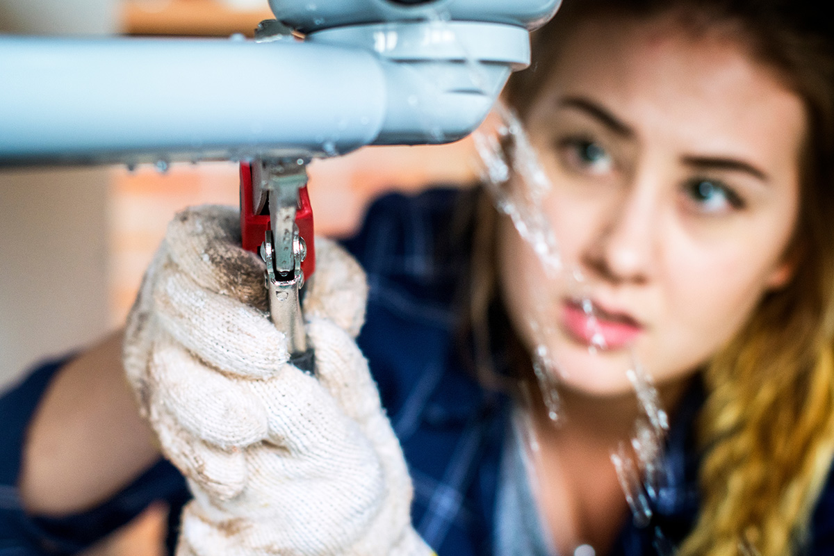 Woman fixing leaking pipe to demonstrate 10 plumbing maintenance tips everyone should know.